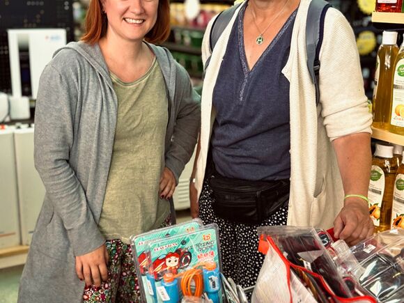 Zwei Frauen beim Einkaufen in einem Laden, stehend neben einem Einkaufswagen, der mit verschiedenen Artikeln gefüllt ist.