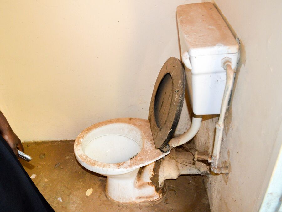An old, dirty toilet in a small room with damaged pipes.