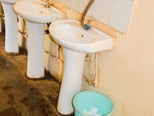 Several sinks in poor condition in a public washroom, with a bucket next to them.